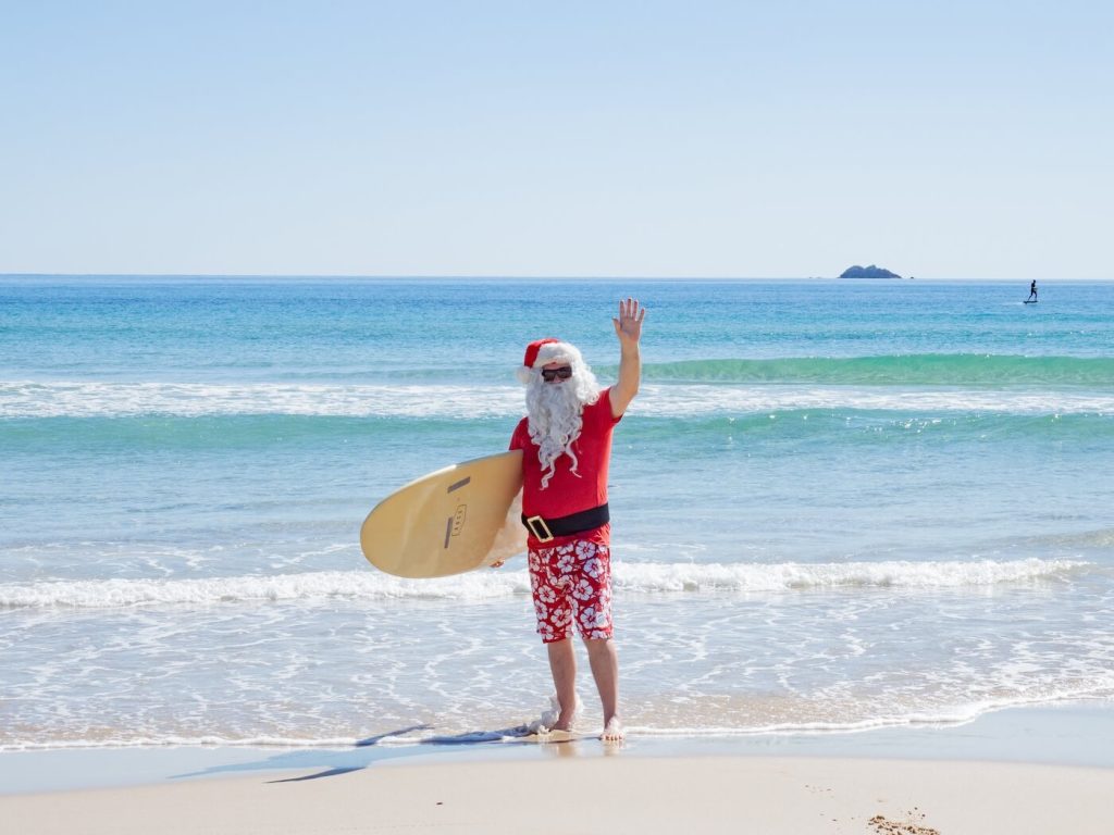 Santa on the beach holding a surfboard