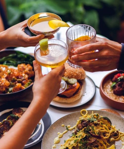 Three people clinking different cocktails at dinner